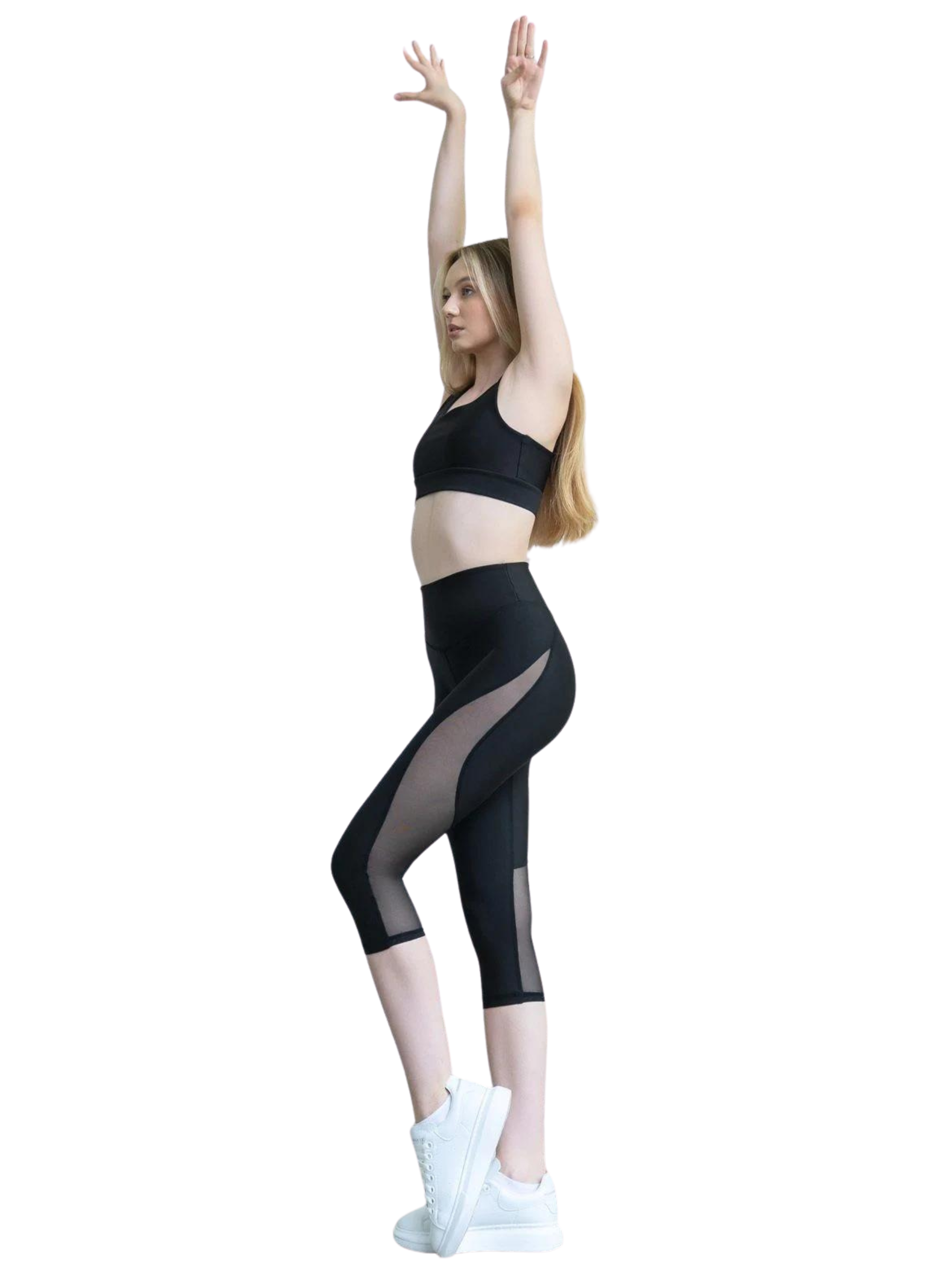 Eine Frau in Lisminas 939 Capri-Leggings in Schwarz streckt sich auf Zehenspitzen vor einem schlichten Hintergrund.